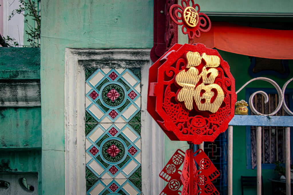 Red and gold Chinese New Year decoration with the character for good fortune, mounted on a green wall.