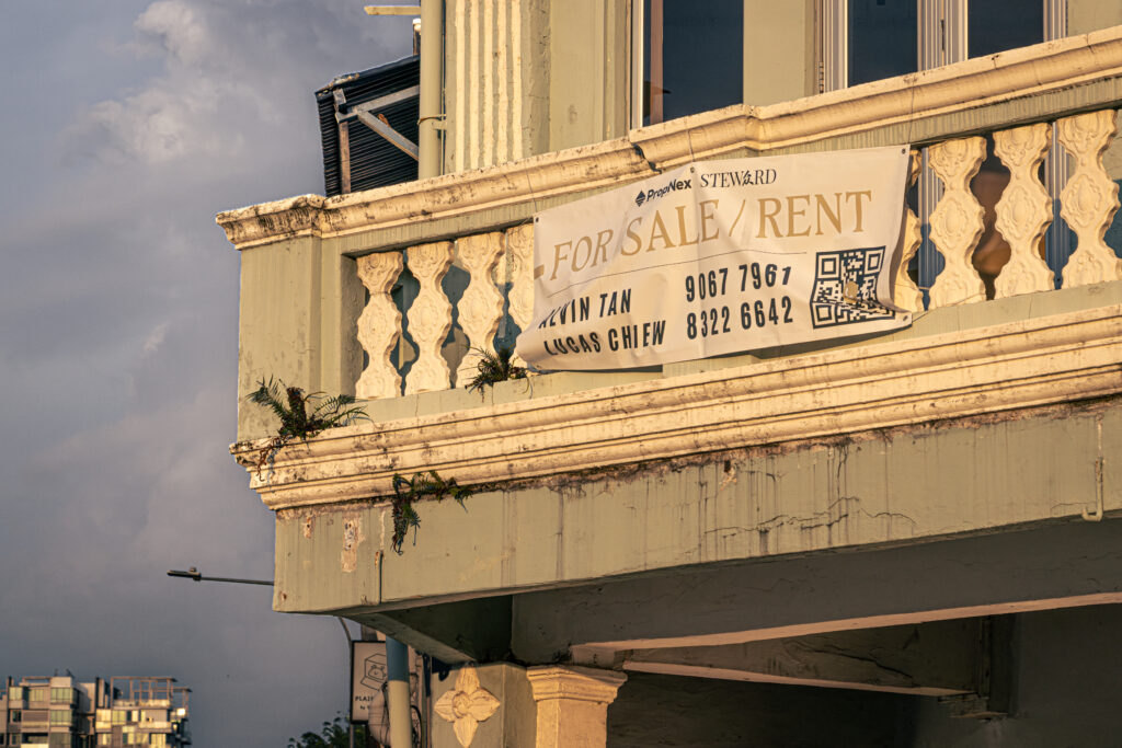 Close-up of a weathered heritage building balustrade with a 'For Sale/Rent' banner, agent contact details, and a QR code.