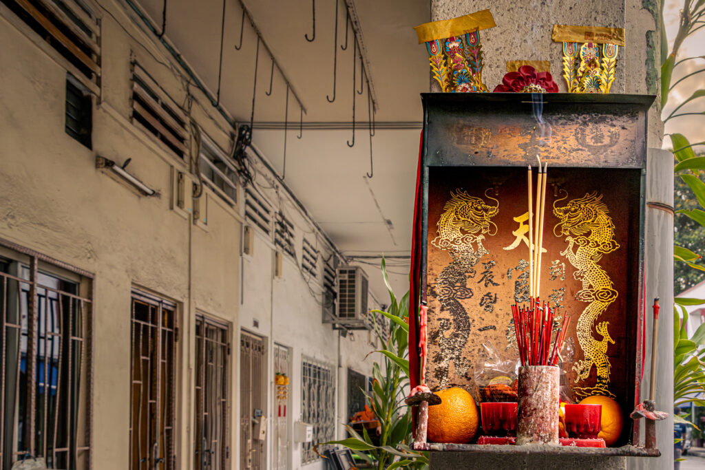 A red wall-mounted incense altar decorated with gold dragon motifs, burning joss sticks, and orange offerings.